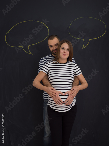 pregnant couple posing against black chalk drawing board