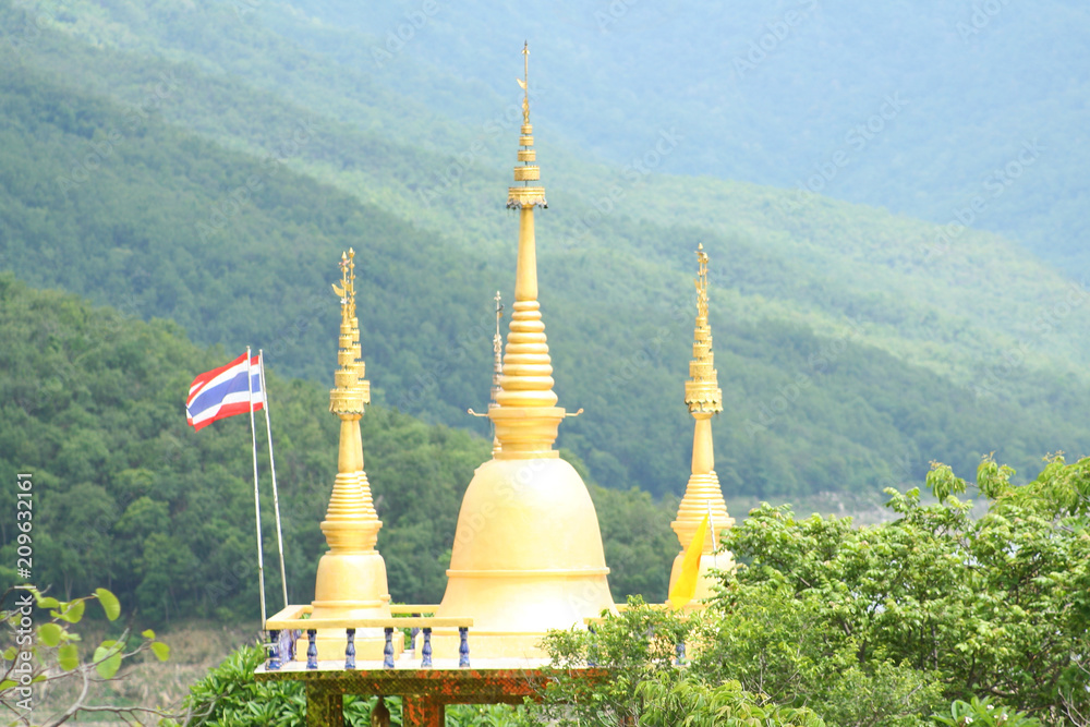 Fototapeta premium Three gloden pagoda and Thailand flag at Phra Phutthabat Pha Nam temple in Tak of thailand in forest mountain background