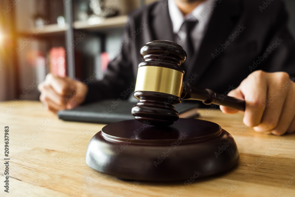 Justice and law concept.Male judge in a courtroom with the gavel,working with,digital tablet computer docking keyboard,eyeglasses,on wood table Justice and law concept.Male judge in a courtroom with the gavel,working with,digital tablet computer docking keyboard,eyeglasses,on wood table