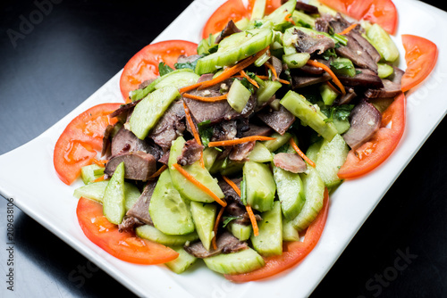 Chinese cuisine, boiled beef with cucumber and tomato in white plate on black background photo