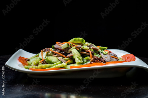 Chinese cuisine, boiled beef with cucumber and tomato in white plate on black background