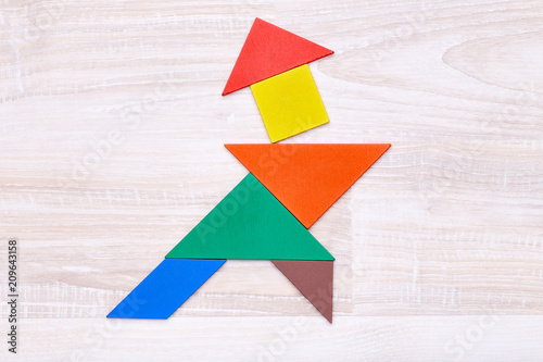 Flay lay of colorful tangram figures arranged in shape of samurai on wooden table.