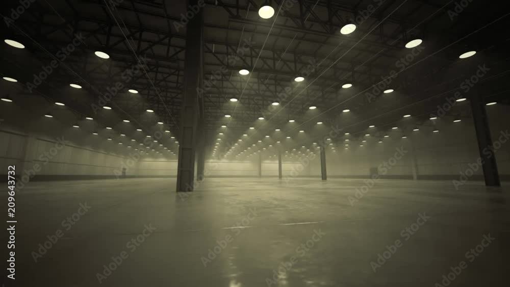 Interior of large, empty industrial warehouse with concrete floor and lamps.