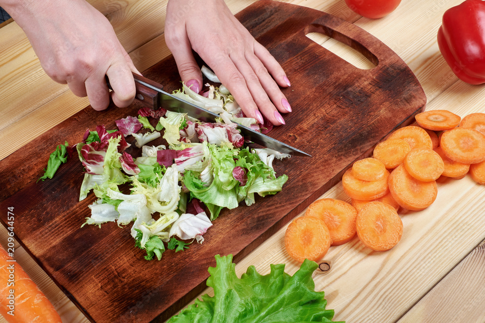 Female hands chopping green salad , cooking vegetables salad on wooden background