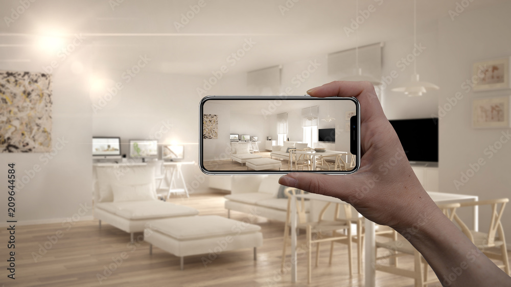 Hand holding smart phone, AR application, simulate furniture and interior design products in real home, architect designer concept, blur background, modern living room with kitchen Hand holding smart phone, AR application, simulate furniture and interior design products in real home, architect designer concept, blur background, modern living room with kitchen