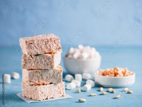 Homemade square bars of marshmallow and crispy rice with ingredients on blue background. Stack of American dessert with marshmallow and crispy rice. Copy space photo