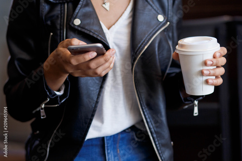 a coarse plan of hands and a white paper cup of coffee. A glass of coffee in hands. Telephone and coffee. The concept of an excellent morning.