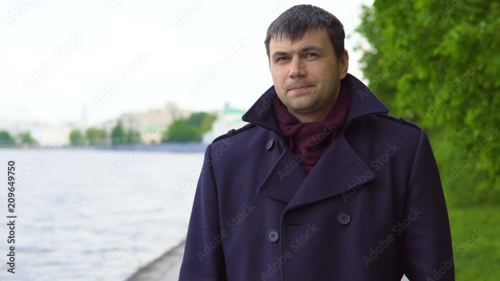 A young man in a black coat walks along the river embankment in the city park. A cloudy spring day. A young man in a black coat walks along the river embankment in the city park. A cloudy spring day.
