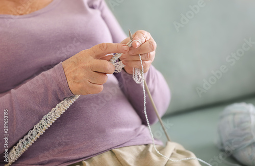 Senior woman knitting sweater at home, closeup