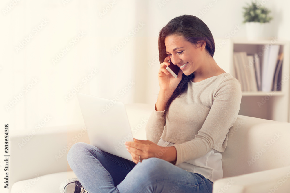 Happy Woman using a laptop and phone on a couch Happy Woman using a laptop and phone on a couch