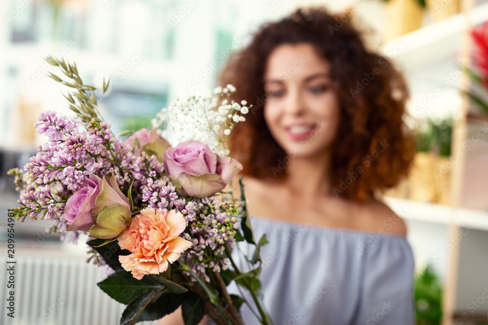 Floristic masterpiece. Selective focus of a flower bouquet being in hands of a cheerful attractive woman