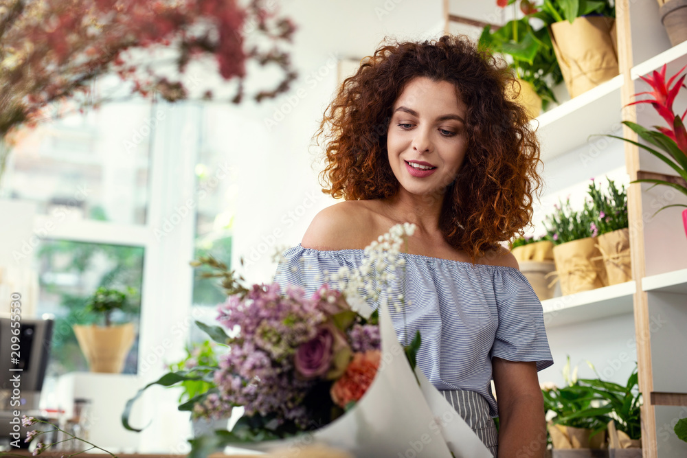 So beautiful. Pleasant attractive woman looking at the flower bouquet while standing in the flower shop