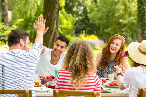 Two friends giving high five while sitting at the table during a garden birthday party with friends