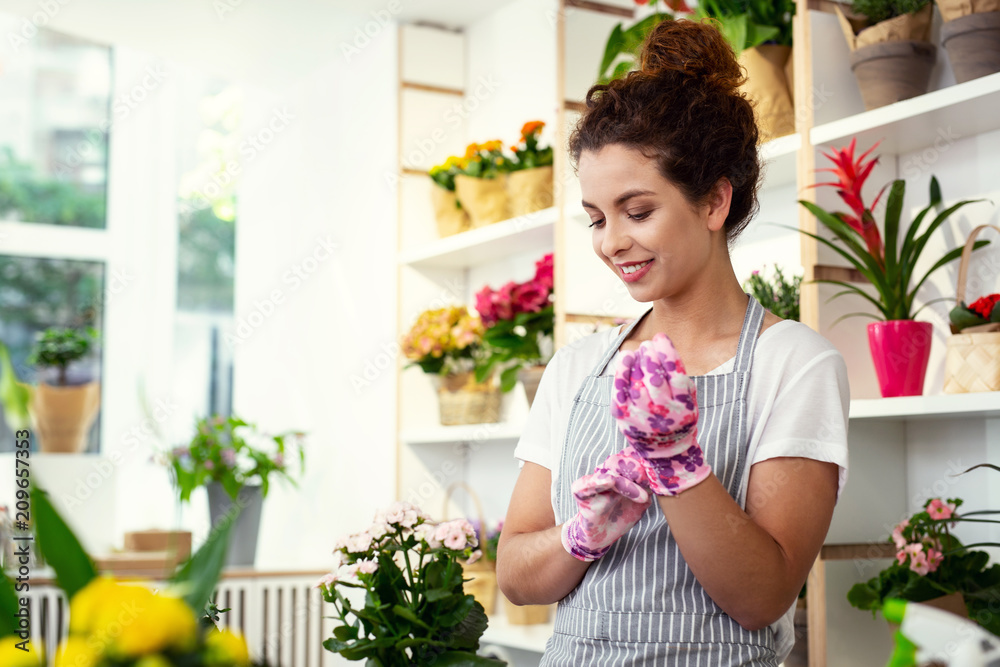 Working accessories. Nice positive woman wearing gloves while working in the flower shop