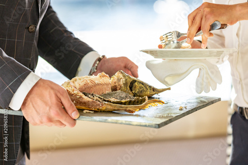 the waiter hands cutting baked sturgeon in the restaurant