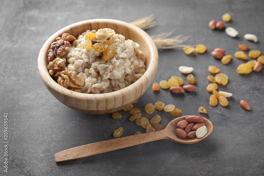 Fototapeta premium Bowl with tasty oatmeal, raisins and nuts on grey background