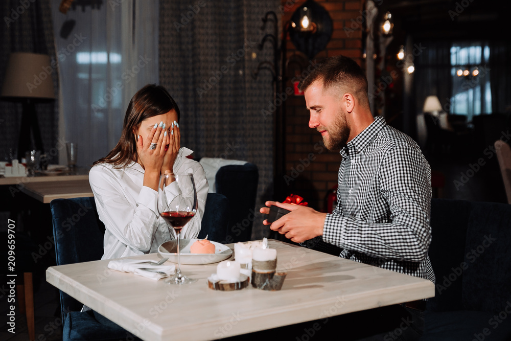 Portrait of happy and surprised young woman receiving present from boyfriend while sitting in cafe
