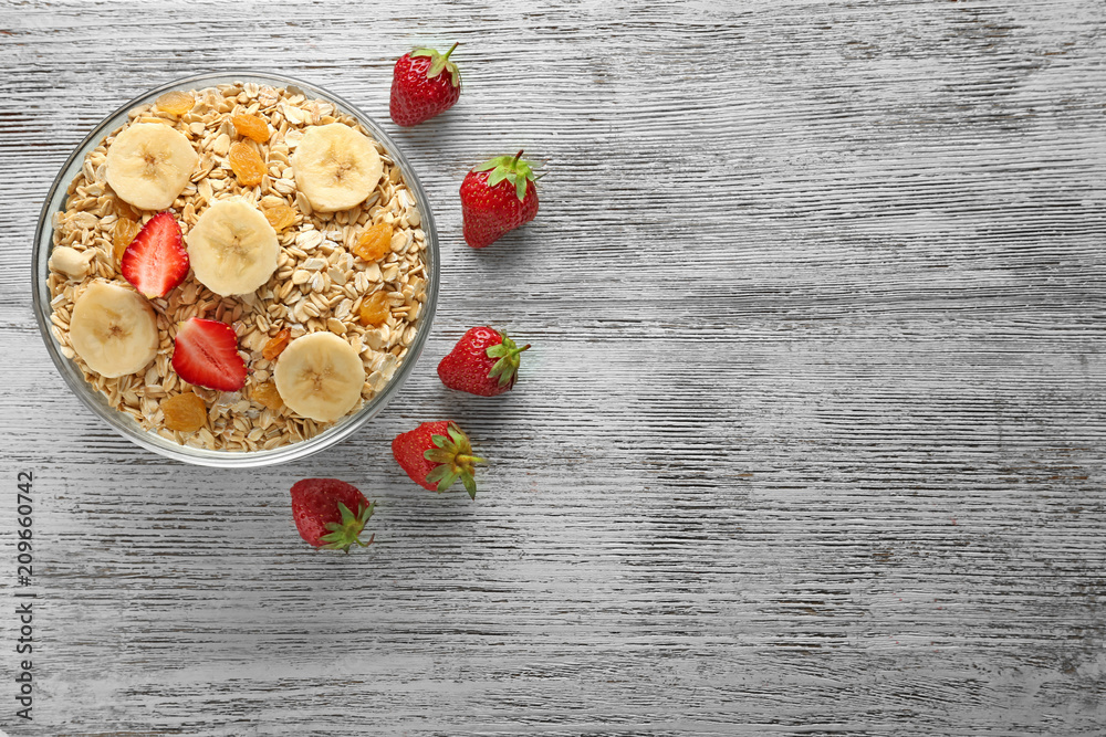 Bowl with raw oatmeal, fruits and berries on wooden table