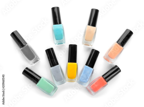 Bottles of colorful nail polish on white background, flat lay