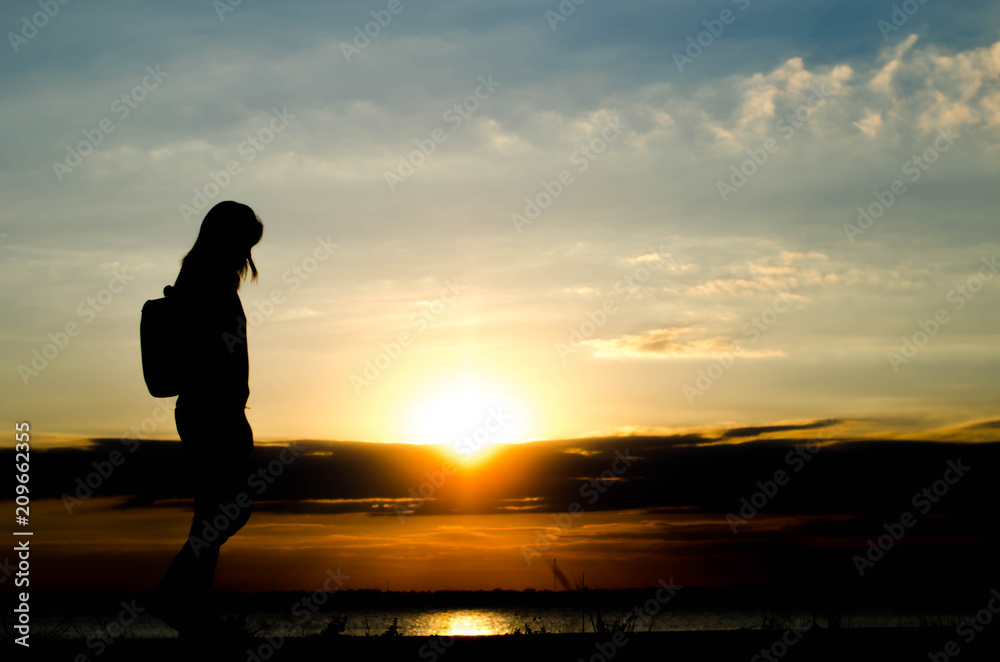 Silhouette of a woman wolking alone at the field during beautiful sunset.