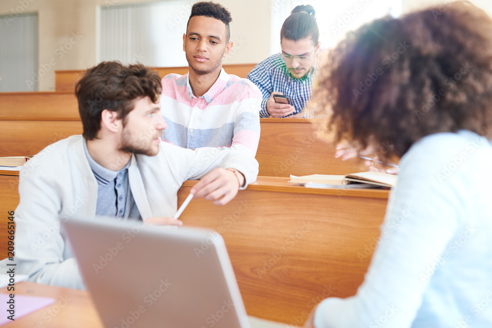 Serious pensive handsome Hispanic student boy in checkered shirt listening to groupmate while they chatting during break in lecture room Serious pensive handsome Hispanic student boy in checkered shirt listening to groupmate while they chatting during break in lecture room