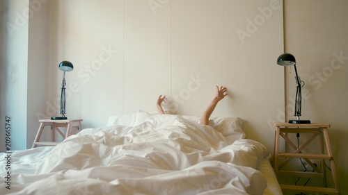 Young Woman is Waking up in a White Bed, Stretching herself and Smiling in the Morning