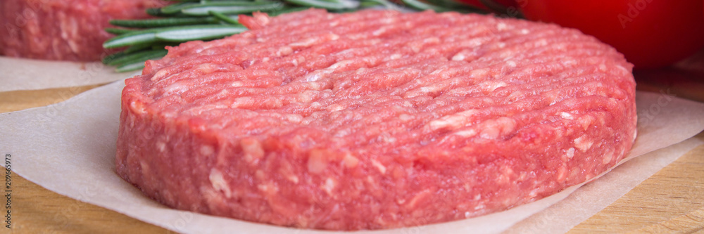 Raw burgers on parchment paper with rosemary and tomatoes. . Banner Raw burgers on parchment paper with rosemary and tomatoes. . Banner