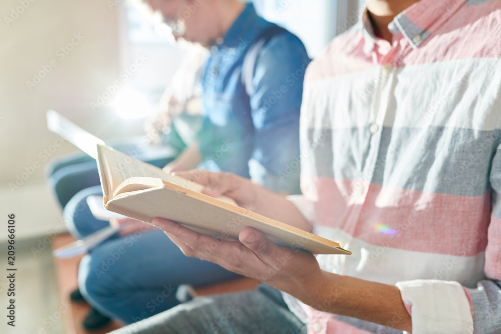 Obraz premium Close-up of unrecognizable students sitting in row and reading textbooks while preparing for exam in corridor