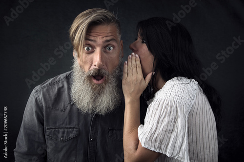 Frau flüstert ihrem Freund ein Geheimnis ins Ohr