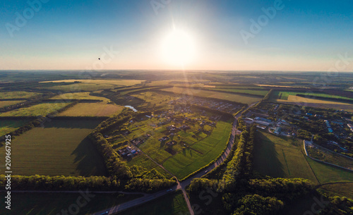 Flight above summer landscape: forest, green fields at countryside in hot air balloon or drone at sunset, aerial view, aerostat travel