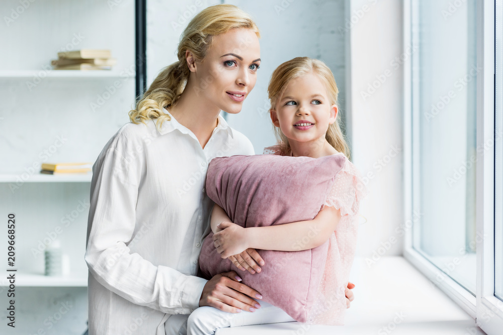 mother and adorable smiling daughter with pillow looking at window at home mother and adorable smiling daughter with pillow looking at window at home