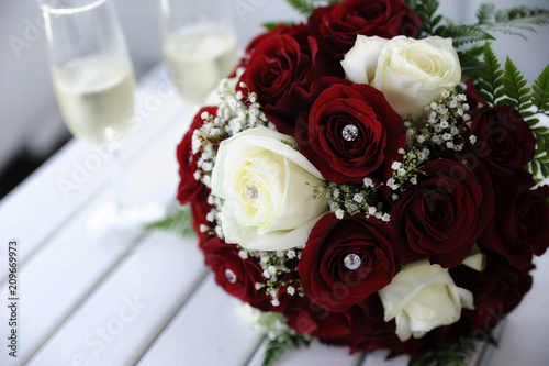 Beautiful red and white roses wedding bouquet on a table with two champagne flutes