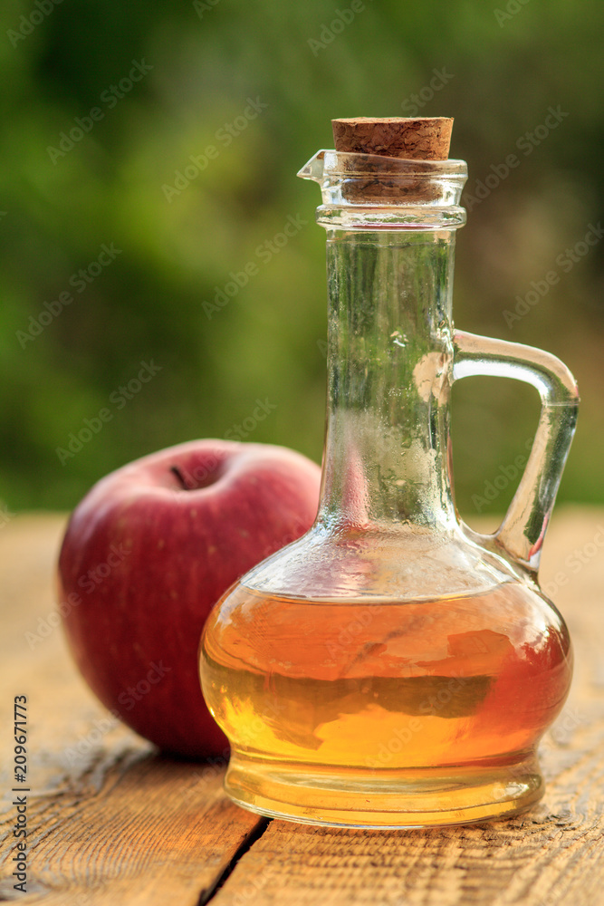 Apple vinegar in glass bottle and fresh red apple on wooden boards with green natural background Apple vinegar in glass bottle and fresh red apple on wooden boards with green natural background