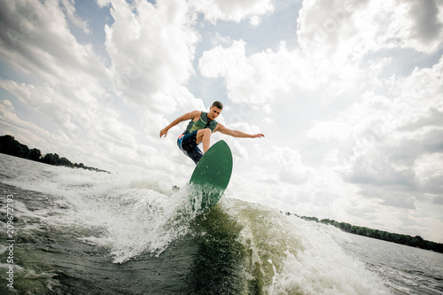 Canvas-taulu Young attractive man riding on the green wakeboard