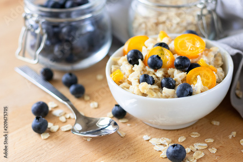 healthy breakfast: oatmeal porridge with blueberries and kumquat, next to a glass jar of blueberries and oatmeal. the concept of diet and healthy lifestyle