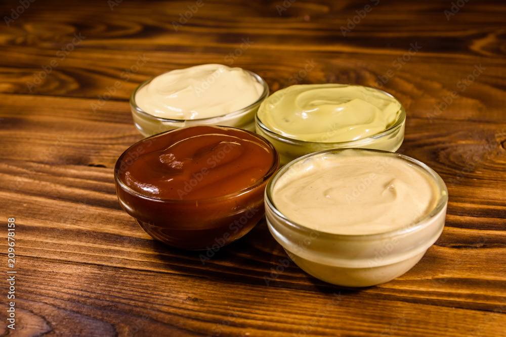Different sauces in glass bowls on wooden table