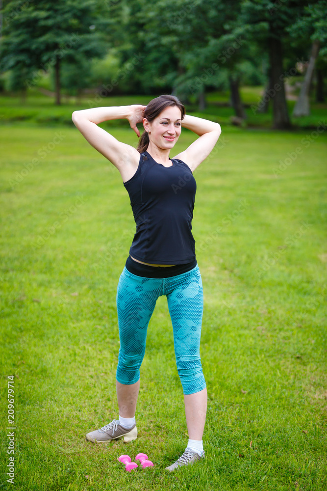 Young woman training with dumbbells in city park at summer day Young woman training with dumbbells in city park at summer day