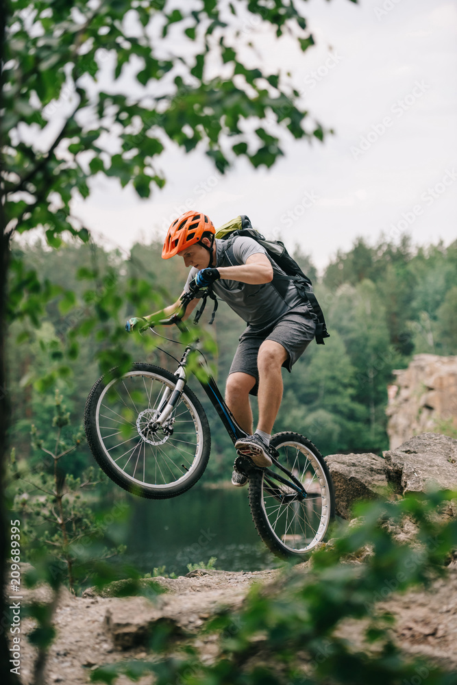 young trial biker performing stunt outdoors in front of forest lake young trial biker performing stunt outdoors in front of forest lake