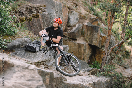 young trial biker relaxing on rocks with bicycle outdoors