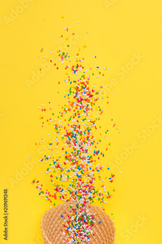 Ice cream cone with colorful sprinkles on yellow background. Closeup, vibrant colors.