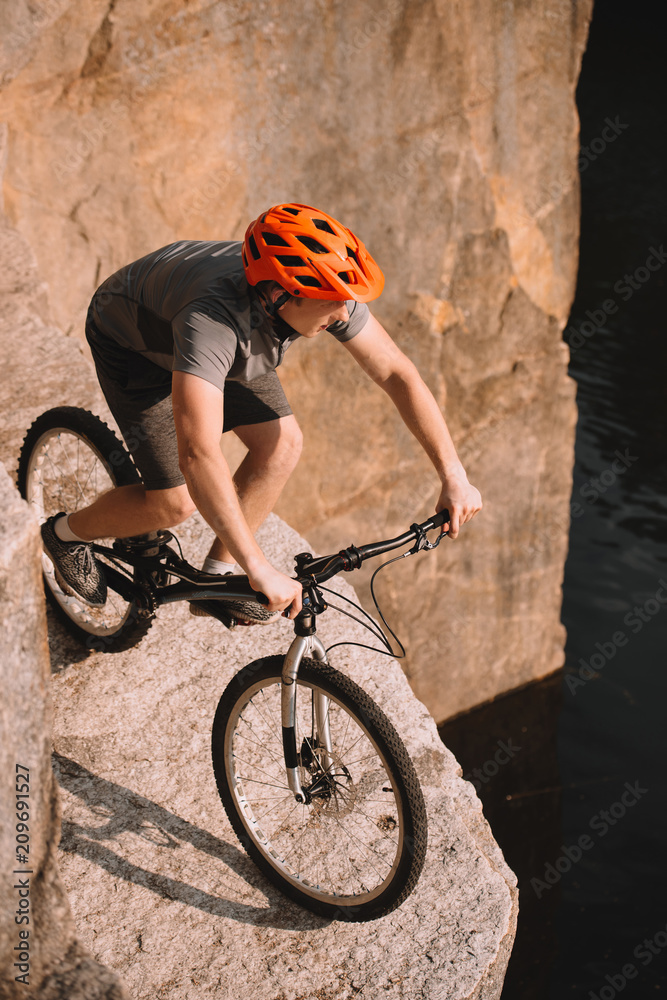 Naklejka premium high angle view of young trial biker balancing on rocks outdoors