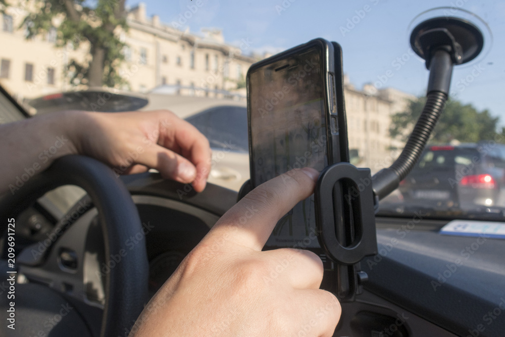 The driver looks at the route in the mobile phone which is fixed on the windshield and is located on a special car holder for the phone