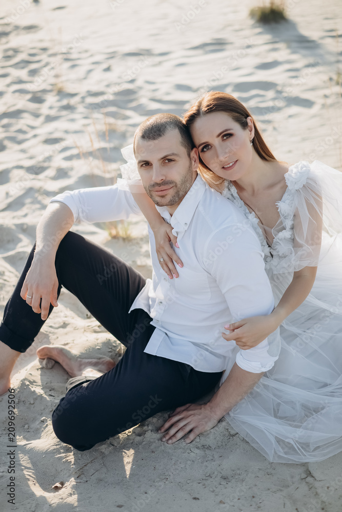 young beautiful couple hugging and sitting on sandy beach