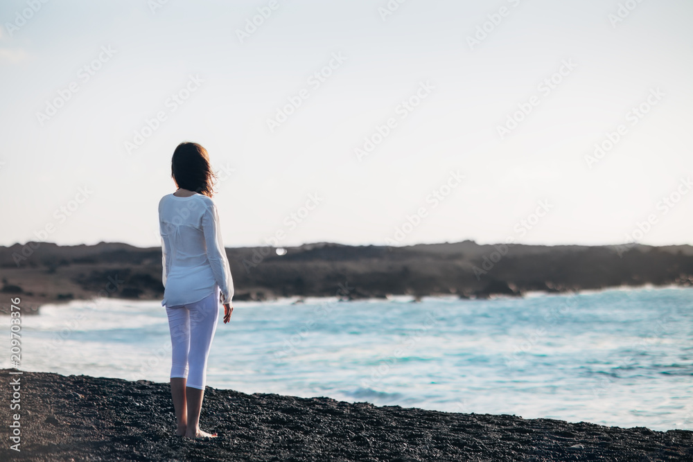 Back view of young lonely woman enjoying ocean on black sand beach Back view of young lonely woman enjoying ocean on black sand beach