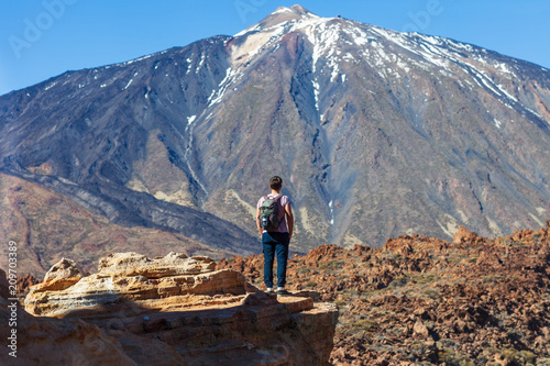 Back view of traveler man standing on the edge of rock looking to volcano El Teide