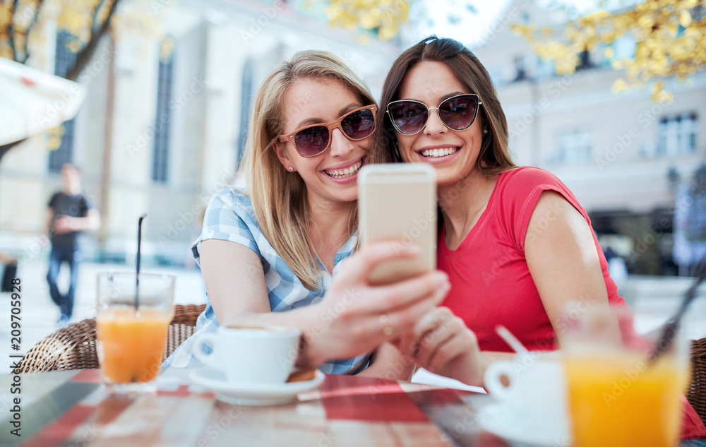 Friends meeting in a cafe. Young women drinking coffee and have fun with mobile phone. Consumerism, lifestyle concept