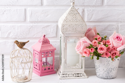 Pink roses  and decorative pink and white lanterns against  white brick wall.