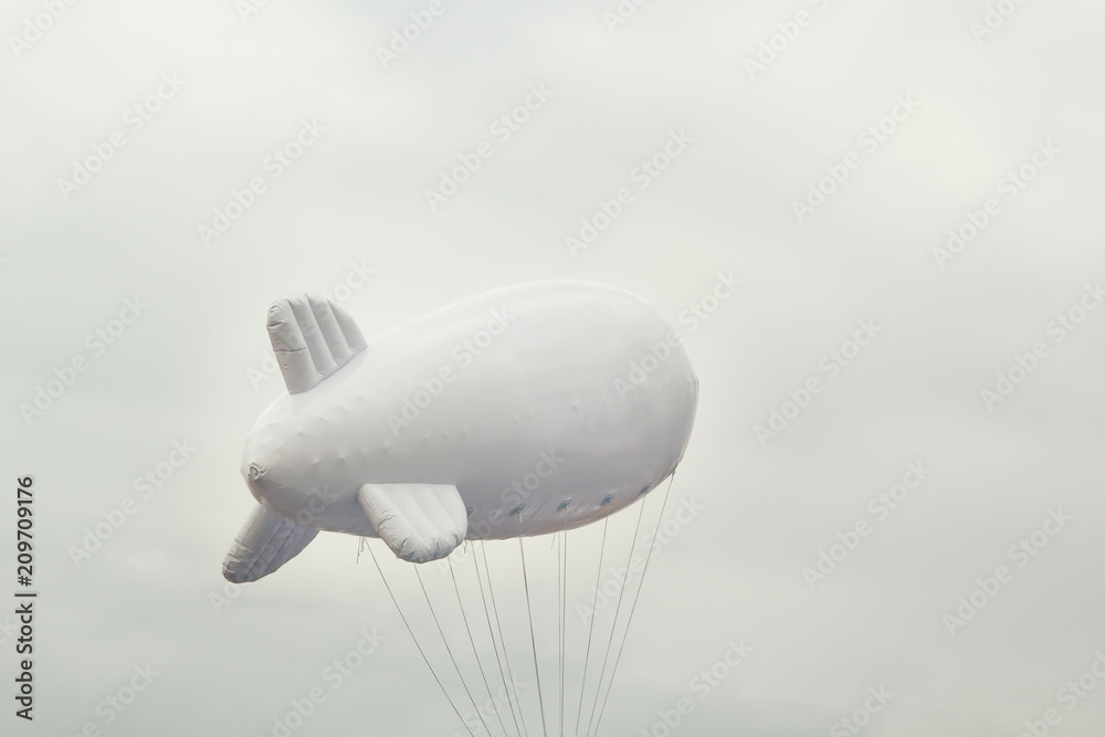Fototapeta premium White inflatable dirigible with a place for a logo on a background of a gray sky with clouds. Copy space