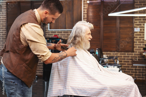 Be attentive. Competent barber standing near his client while modelling new hairdo
