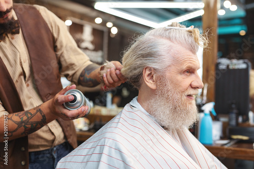 Using spray. Professional male hairdresser holding bottle with spray while using it for fixing hair © zinkevych